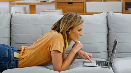 Close Up Of Young Woman At Home Lying On Sofa Using Laptop Computer For Work Or Browsing Online