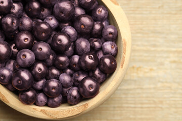 Ripe acai berries in bowl on wooden table, top view. Space for text