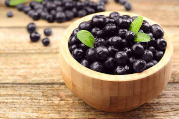Ripe acai berries and leaves in bowl on wooden table, closeup. Space for text