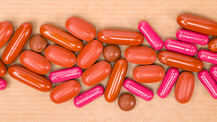 close up of red and pink pills on a wooden background, top view