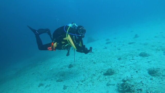 A good-trimmed Scuba Diver at a wreck dive in Puerto Galera, Philippines. A school of batfish is in the background. Video light toward the camera