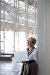 Middle-aged businesswoman reflects while working on a laptop in a modern office environment during daytime hours