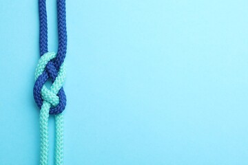Colorful ropes tied in knot on light blue background, top view with space for text. Unity concept