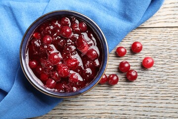 Tasty cranberry sauce in bowl and berries on wooden table, top view