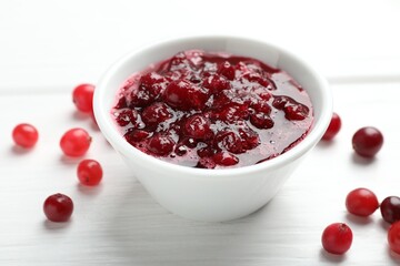 Tasty cranberry sauce in bowl and berries on white wooden table, closeup