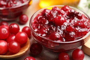 Tasty cranberry sauce in glass bowl and berries on table, closeup