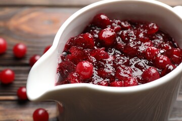 Tasty cranberry sauce in gravy boat and berries on table, closeup