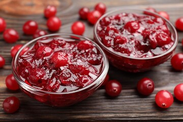 Tasty cranberry sauce in glass bowls and berries on wooden table, closeup