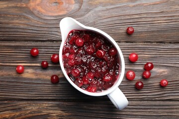 Tasty cranberry sauce in gravy boat and berries on wooden table, top view