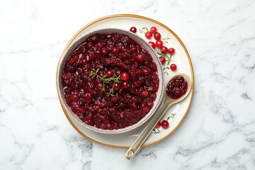 Tasty cranberry sauce in bowl, berries, thyme and spoon on white marble table, top view