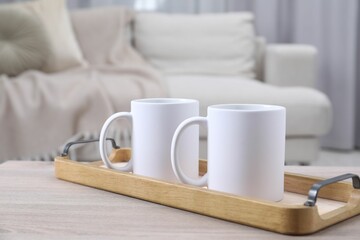 Blank ceramic mugs on white wooden table indoors. Mockup for design