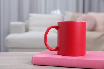 Blank red ceramic mug and notebook on wooden table. Mockup for design