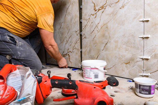 Tilers installing large format tiles on wall.
