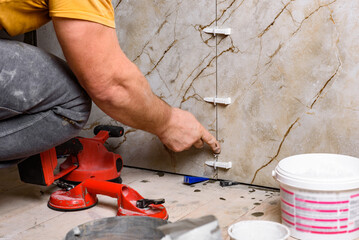 Tiler installing leveling system tiles on wall.