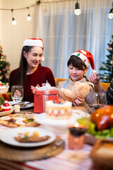 Asian joyful holiday gathering featuring a woman and a child in festive hats, enjoying food and gifts in a warmly decorated in winter Xmas party