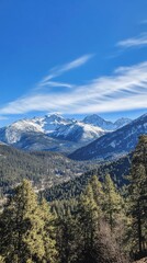 Obraz premium Majestic snow-capped mountains rise under a clear blue sky, surrounded by lush green forests and distant peaks at sunrise