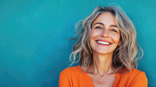 Cheerful beautiful mature woman with a vibrant smile standing against a blue background .Close up portrait of beautiful older woman smiling and standing by wall