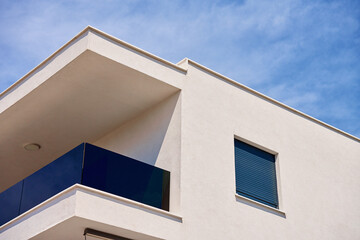 Close-up of modern apartment building with glass balconies against bright blue sky. Abstract view of residential building in minimalist style. Detail of contemporary architecture