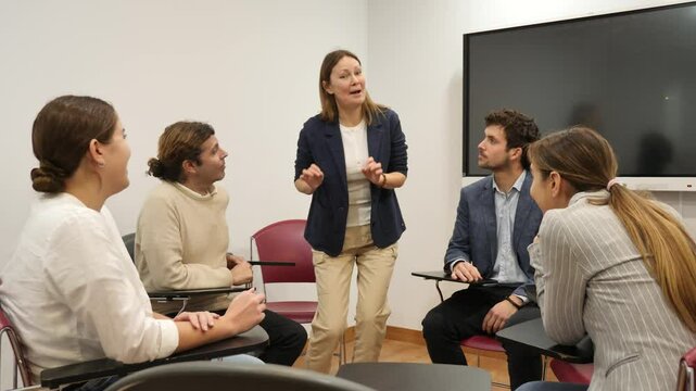 Friendly businesswoman standing near interactive board and communicating with group of adult students at seminar in advanced training