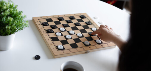 Close-up of hand moving a black checker piece on wooden checkerboard. The board features...