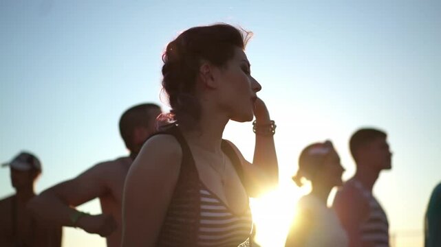 Yong Asian Woman with bright make up dancing singing, waving hands at music concert on open air fest. Crowd applause, jump, enjoy favourite band performance on stage. Hard rock punk gig. Sunset summer