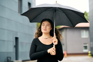 A young plus size woman strolls gracefully, holding an umbrella on a beautiful autumn day outdoors.