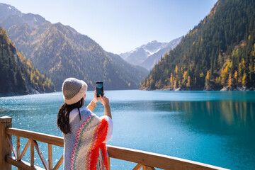 Young female tourist enjoying and taking a photo at beautiful autumn scenery landscape at jiuzhaigou national park in Sichuan, China