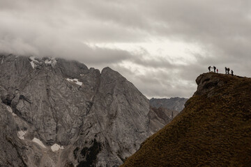 Silhouettes of hikers pause on a cliffside, gazing over the sweeping alpine landscape of the...