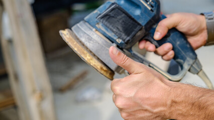A middle-aged man sanding timber with a sander in the garden of his house on a summer day