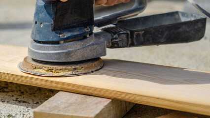 A middle-aged man sanding timber with a sander in the garden of his house on a summer day