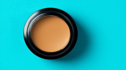 A round container of foundation sits against a vibrant turquoise background, showcasing its creamy texture and natural shade.