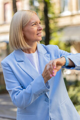 Fototapeta premium Serious sad businesswoman standing outdoors looking around waiting for business meeting impatient woman dissatisfied looks at wristwatch, checks time on watch annoyed by being late lateness concept.
