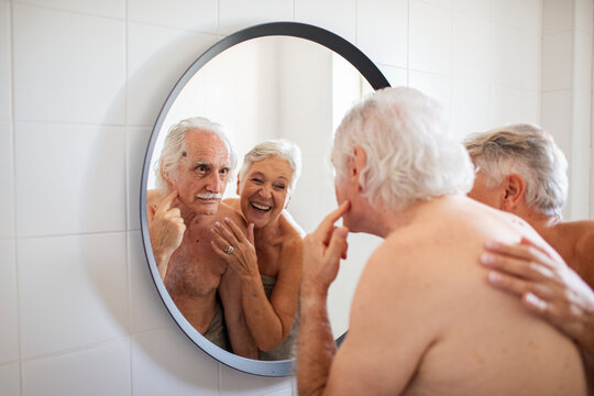 Elderly couple sharing a playful moment in front of the bathroom mirror