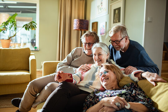 Group of senior friends laughing while taking selfie together at home