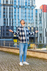 Mature man meditating with closed eyes standing on downtown city street. Calm middle-aged male tourist with arms out rests and feels peace of mind. Guy relaxes to relieve stress against building.