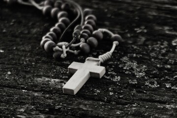 Wooden rosary with cross on rustic wooden table black and white