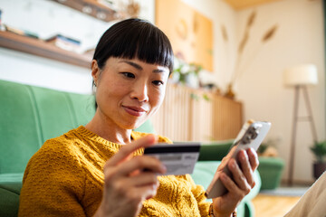 Woman making online payment with credit card and smartphone at home