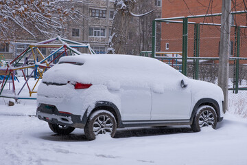 Car covered with snow on the playground in the city in winter.