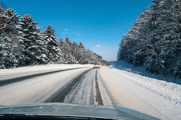 A car drives down a road lined with snow-covered trees.