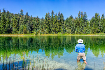 Eagle County Emerald Lake with coniferous trees and mirror sky reflection on water surface and man fishing with rod