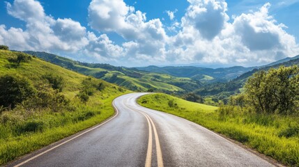 Naklejka premium Scenic winding road through lush green hills under a bright blue sky with fluffy clouds on a sunny day