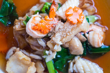 Wide rice noodles with seafood in gravy sauce, or Thai called Rad Na Taley are served on a white plate in the restaurant.