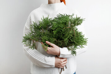A woman in a white sweater holding thuja branches, symbolizing winter and natural beauty