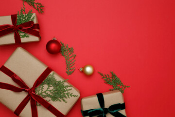 Gifts wrapped in craft paper, Christmas ornaments, and thuja branches arranged on a red background