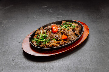 Sizzling beef liver with onions and fresh greens served on hot plate, perfect for a hearty meal