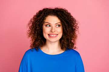 Fototapeta premium Young woman with curly hairstyle in blue sweatshirt against a pink background, looking joyful and confident