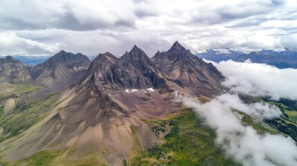 Fototapeta premium Breathtaking Aerial View of Rugged Mountain Range Surrounded by Clouds and Green Valleys under a Dramatic Moody Sky in Nature's Landscape