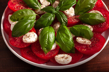 Fresh Caprese salad of sliced tomatoes, mozzarella and basil on a rustic wooden table. Healthy Mediterranean cuisine. The concept of healthy vegetable dishes. Good nutrition 