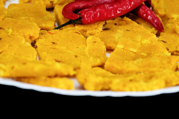 Isolated against a black background, Gujarati Kathiyawadi Spicy Dhokali Sabji is seen with red chillies on top of a white plate