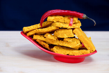 Side view of Gujarati Kathiyawadi Spicy Dhokali Sabji with a red chilli sitting atop a bowl. The stunning black backdrop highlights the red dish's distinctive features